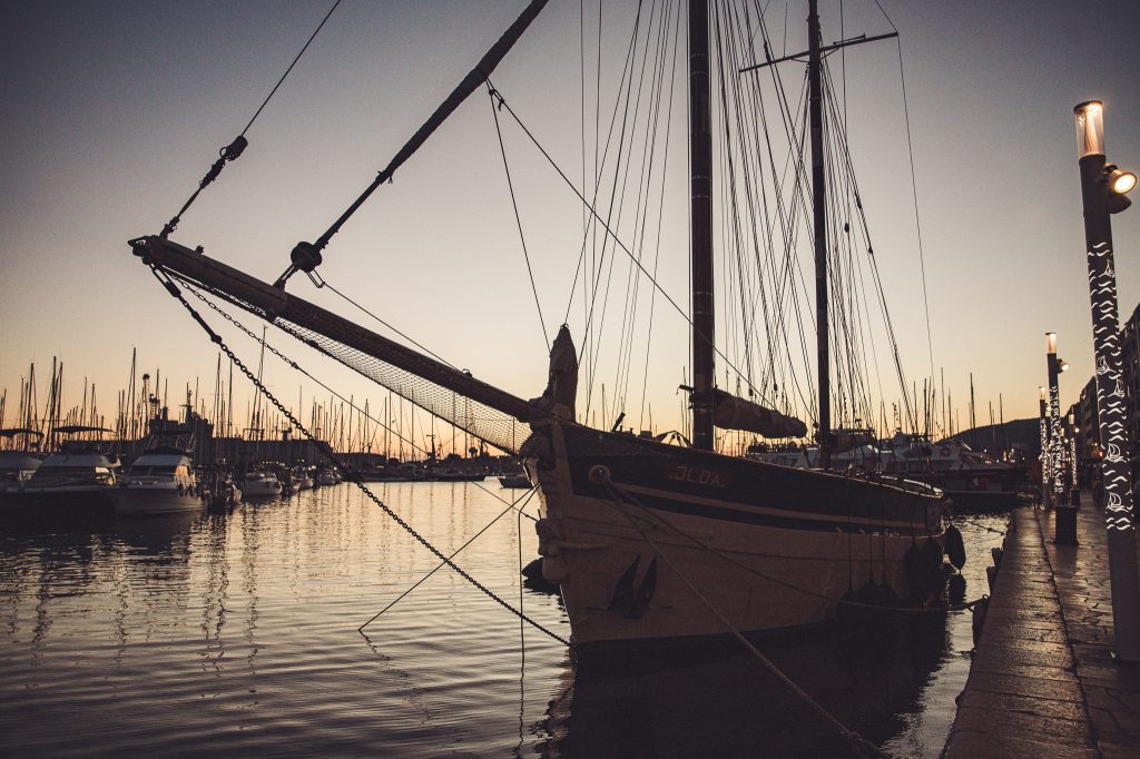 Historisches Segelschiff und beleuchtete Hafenpromenade bei Sonnenuntergang in Südfrankreich