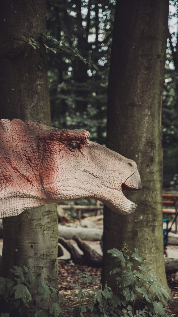 Nahaufnahme des Kopfes einer lebensgroßen Dinosaurierfigur zwischen Bäumen im Zoo Osnabrück