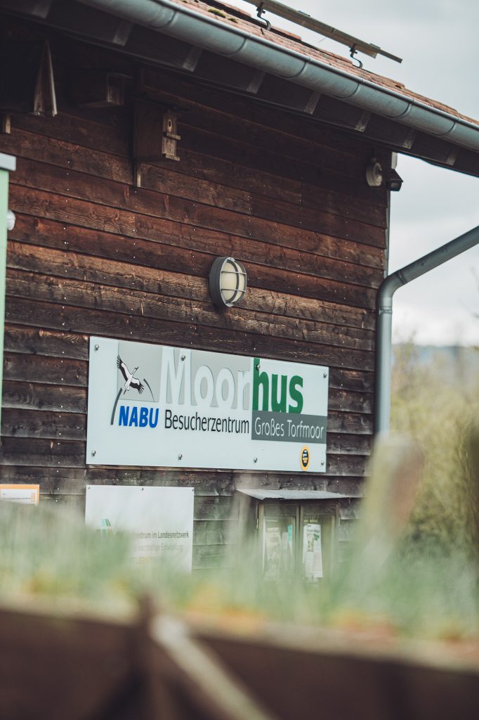 Schild des NABU Besucherzentrums Moorhus an einer dunklen Holzfassade