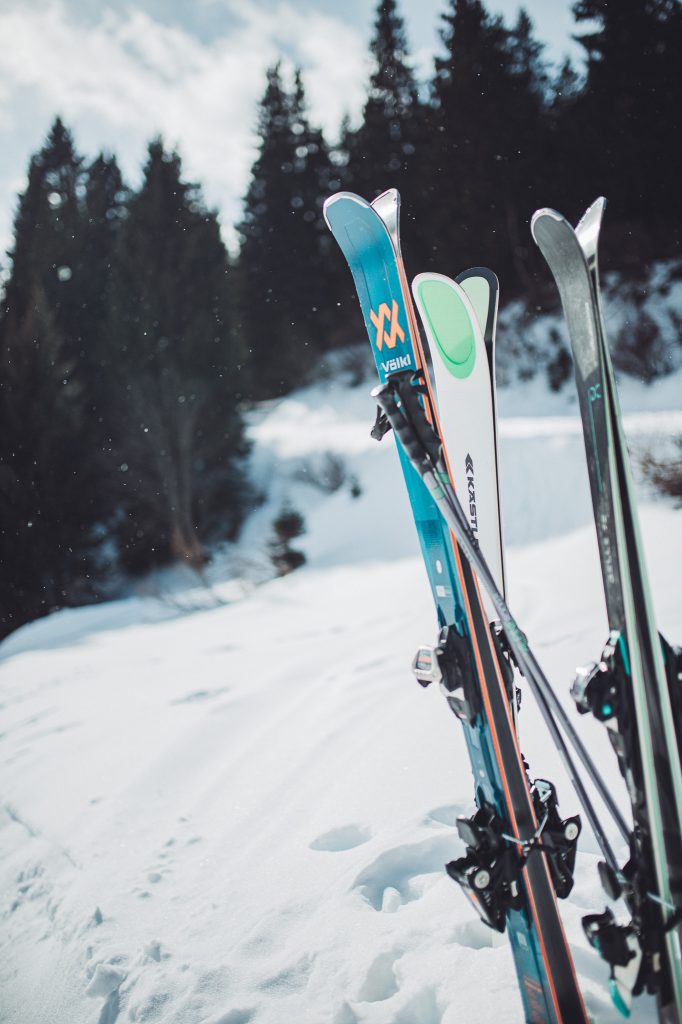 Mehrere aufrecht stehende Ski vor einem verschneiten Hang mit Nadelbäumen