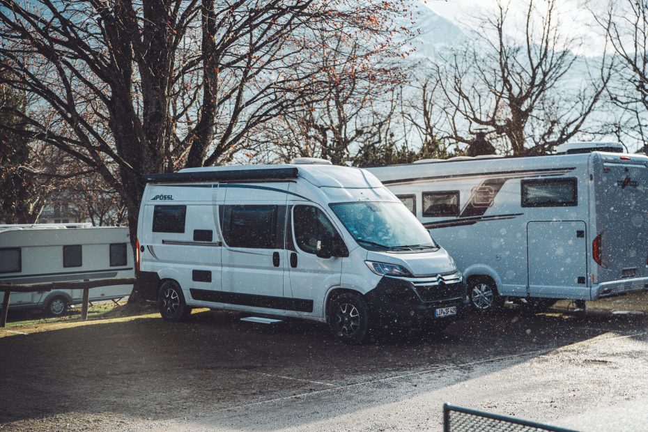 Weißer Kastenwagen neben einem Wohnmobil und einem Wohnwagen unter kahlen Bäumen auf dem Campingplatz Alpenblick bei Interlaken.