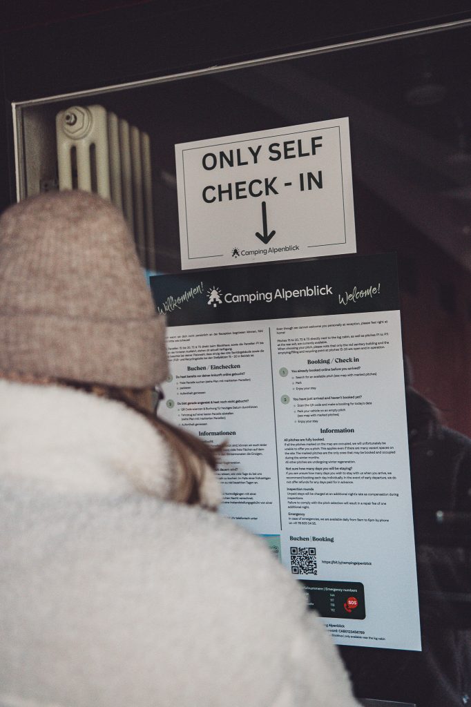 Person mit Strickmütze vor den Aushängen zum Self Check-in am Campingplatz Alpenblick bei Interlaken.