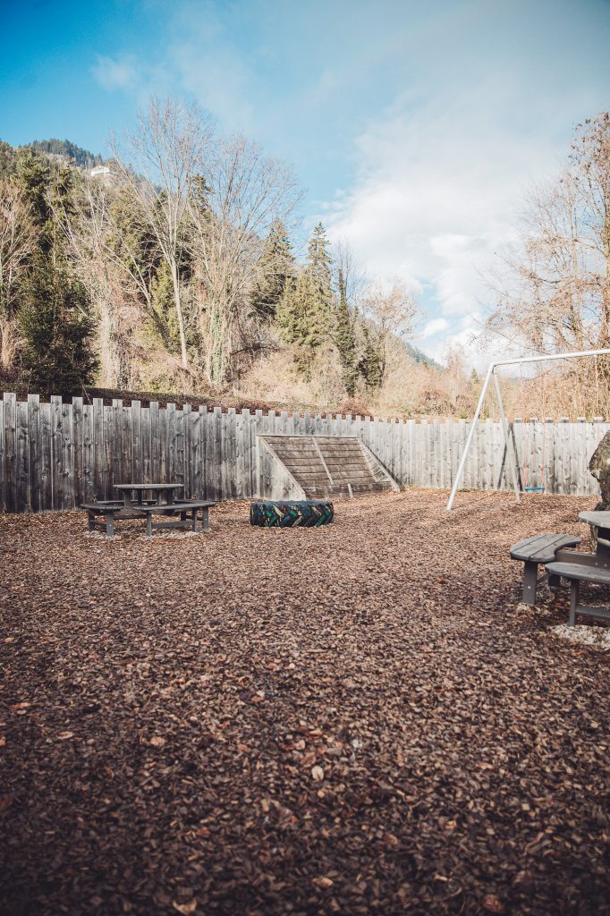 Spielplatz mit Schaukel, Holztischen und buntem Reifen vor einem Holzzaun neben dem Campingplatz Alpenblick bei Interlaken.