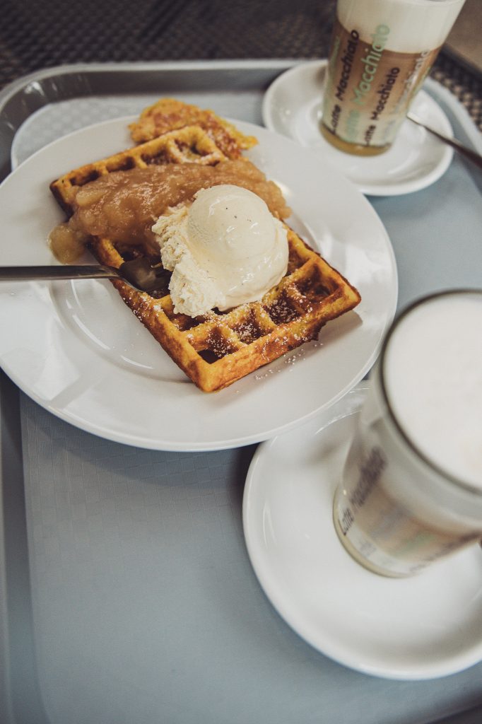 Kürbiswaffel mit Vanilleeis und Apfelkompott neben zwei Gläsern mit warmen Milchgetränken