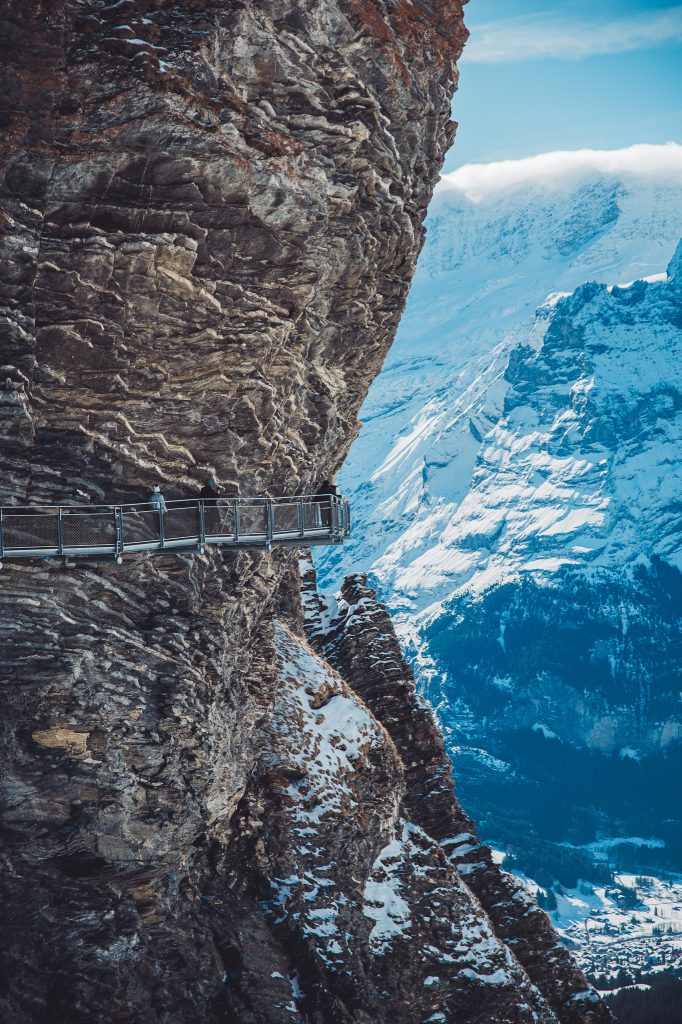 Menschen auf dem schmalen Metallsteg des First Cliff Walk an einer steilen Felswand über Grindelwald