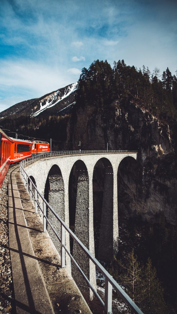Roter Zug der Rhätischen Bahn auf dem gebogenen Landwasserviadukt mit hohen steinernen Pfeilern