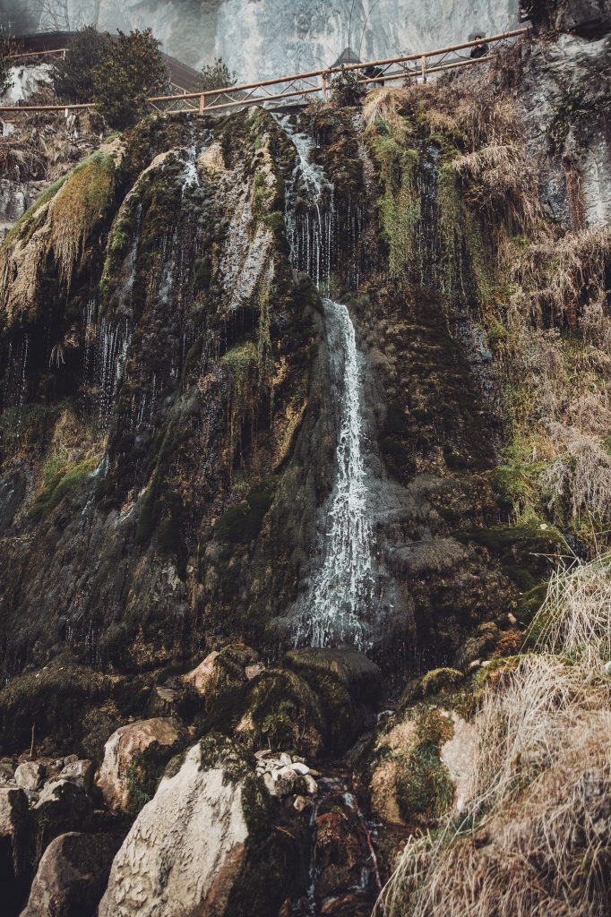 Wasserfall über moosbewachsene Felsen unter einem Weg mit Holzgeländer an den St. Beatushöhlen