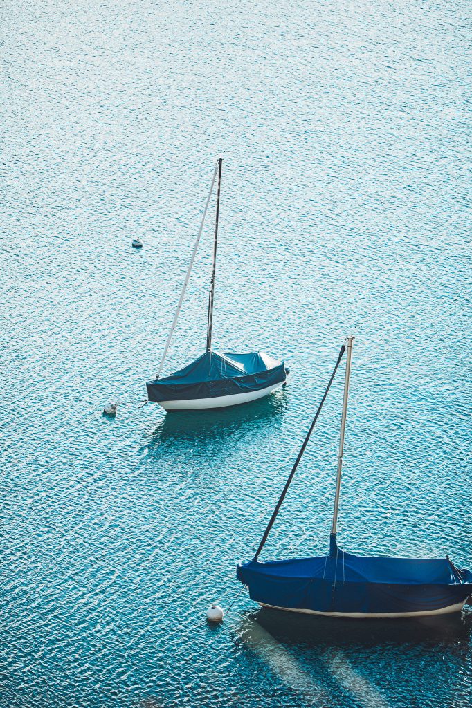 Zwei mit blauen Planen abgedeckte Segelboote an Bojen auf dem türkisblauen Thunersee